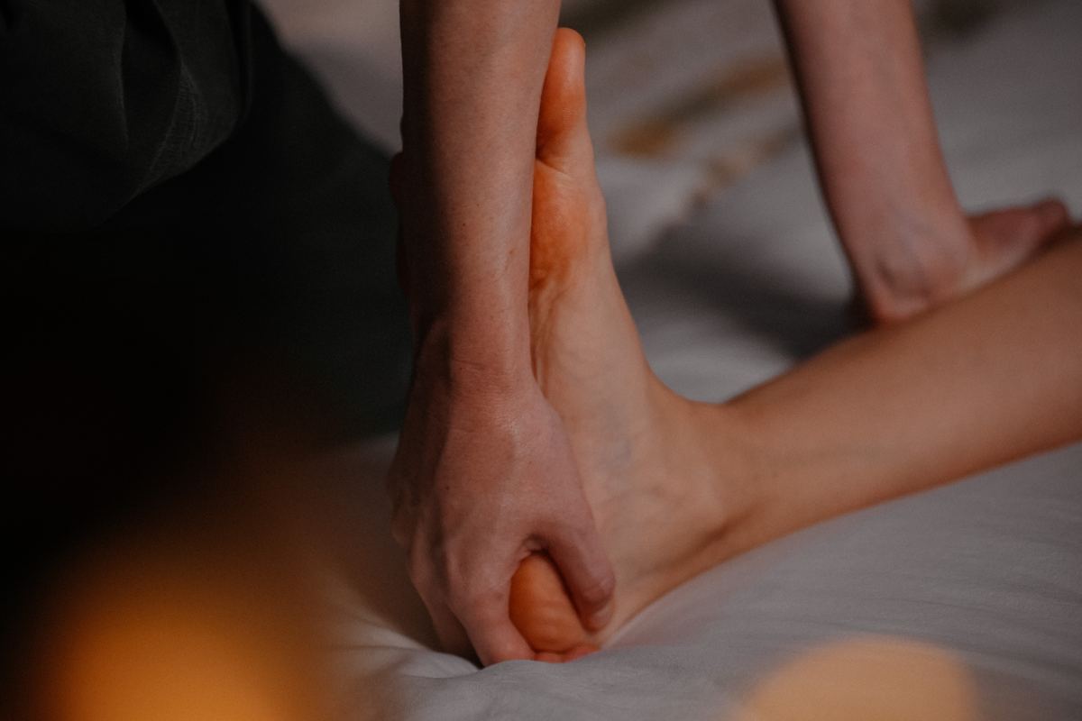 Kira working on a client’s foot with a wooden tool in candlelight