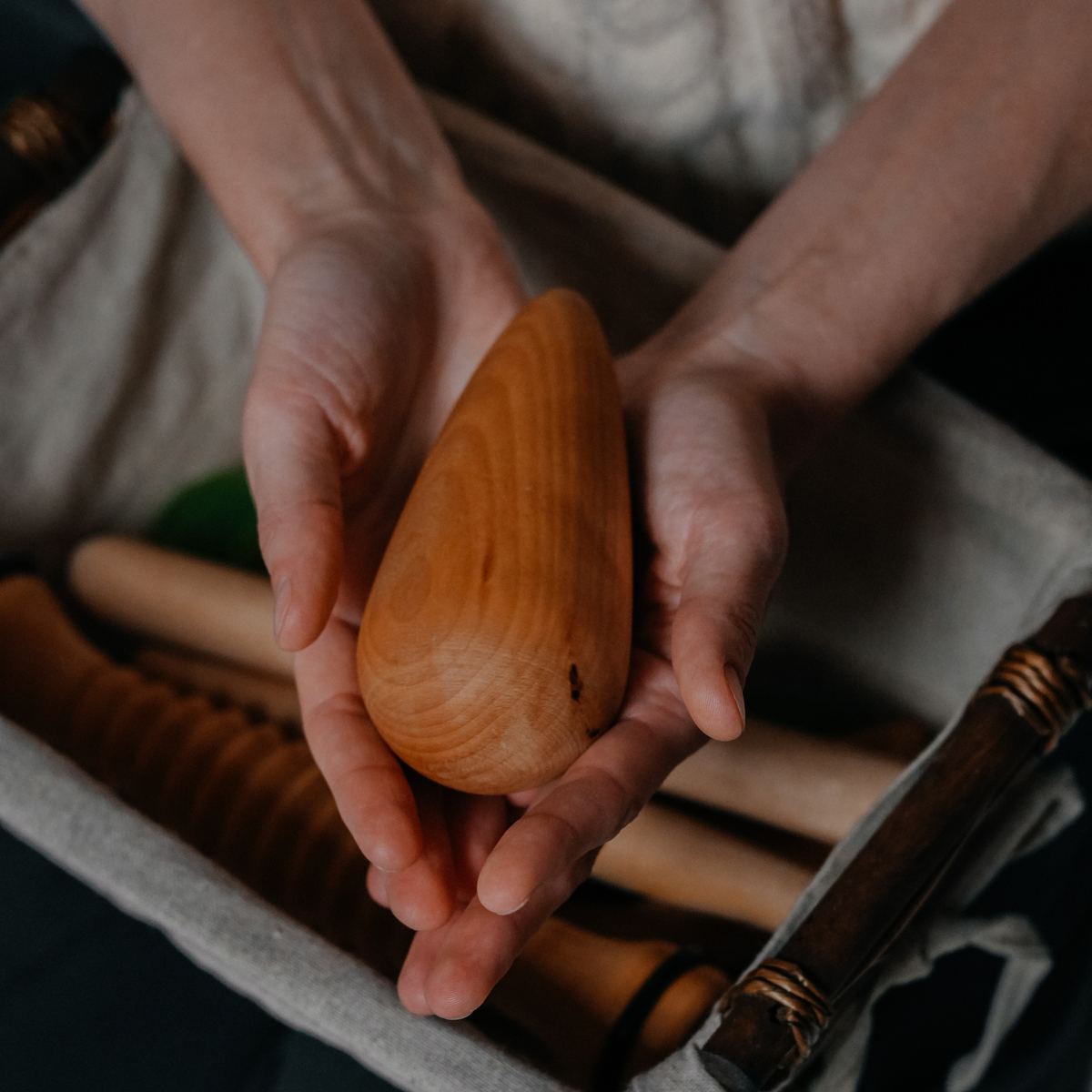 A wooden drop for Slavic bodywork held in Kira’s hands over a basket of wooden tools